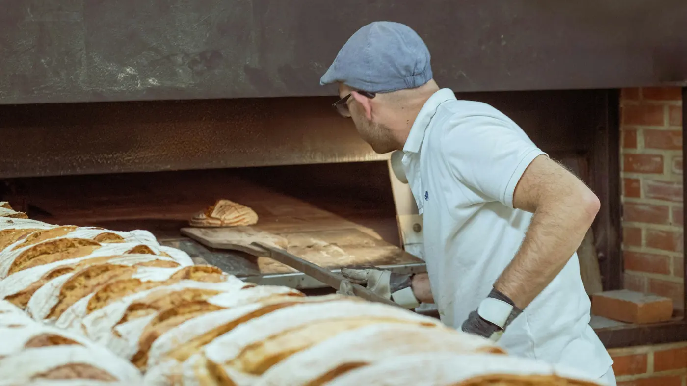 A baker pulling loaves from the oven